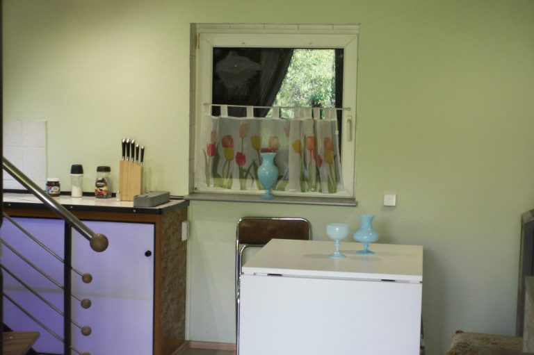 Küche mit grünem Wandfarbton, Fenster mit Vorhang und Geschirr auf der Theke.