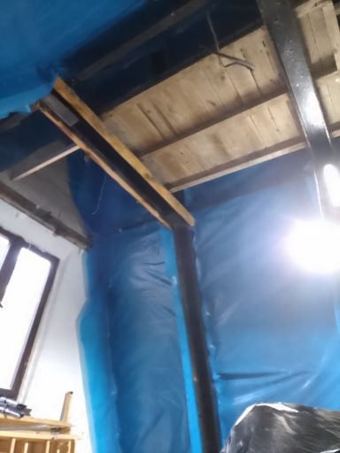 Raum mit blauen Kunststofffolien, Holzträgern und einer Decke aus Holz und Metall.