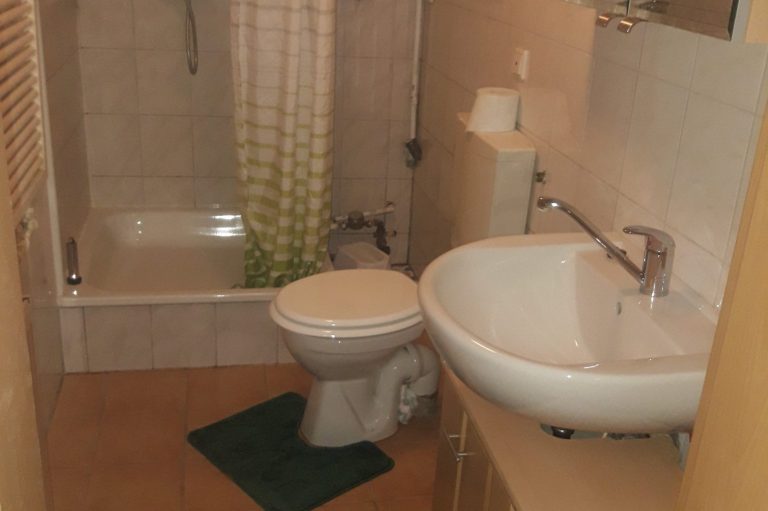 Kleines Badezimmer mit Dusche, Toilette und Waschbecken auf Fliesenboden.