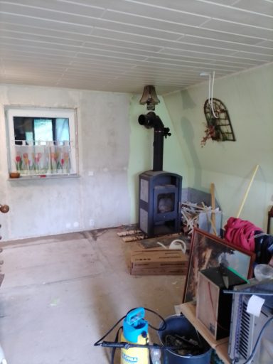 Ein unordentlicher Raum mit einem Ofen, Fenster und verschiedenen Gegenständen.