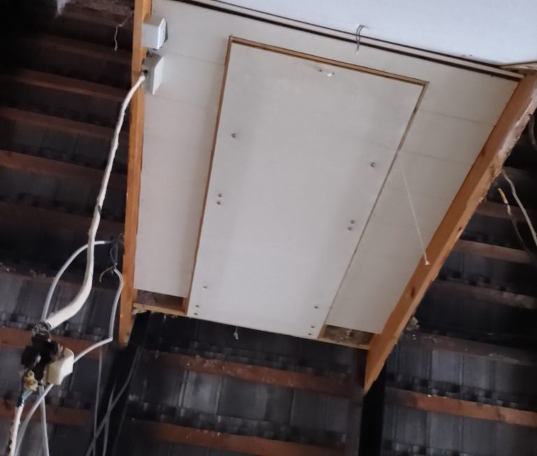 Luke Decke mit einem weißen Panel und sichtbaren Kabeln, Holzrahmen sichtbar.