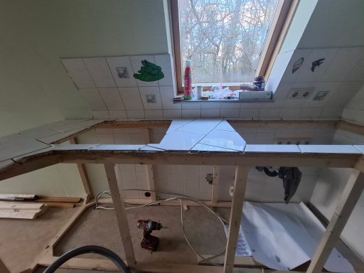 Unvollendete Küchenecke mit Holzrahmen und gefliester Wand, Baustellenutensilien sichtbar.