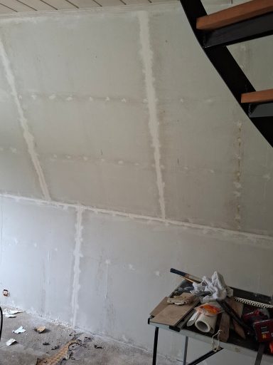 Rohbau mit verputzter Wand und Treppe, Baustelle mit Werkzeugen.