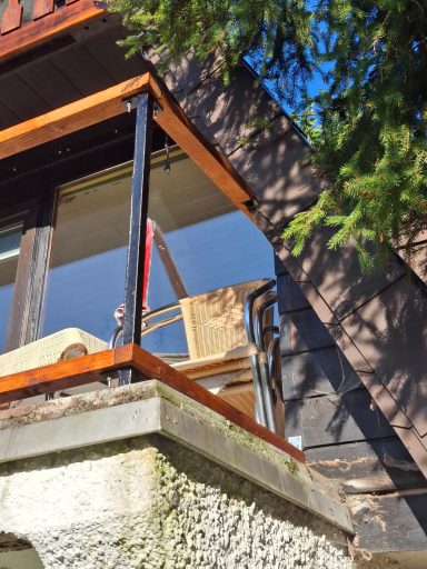 Ein Holzgeländer mit einem Stuhl und einer Leiter, beleuchtet von Sonnenlicht.