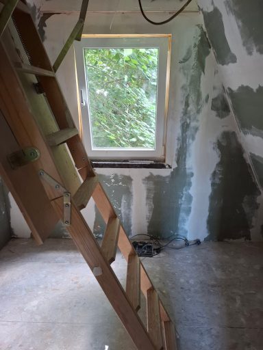 Holzleiter in einem unfertigen Raum mit einem Fenster und unvollendeten Wänden.
