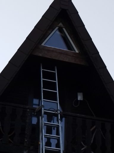 Haus mit Spitzdach, Leiter an der Wand und Fenster im Giebelbereich.