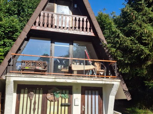 Ein modernes Ferienhaus mit Balkon, umgeben von Bäumen und klarem Himmel.