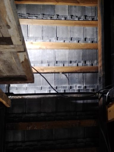 Dunkler Raum mit Holzlatten und einer beleuchteten Wand im Hintergrund.