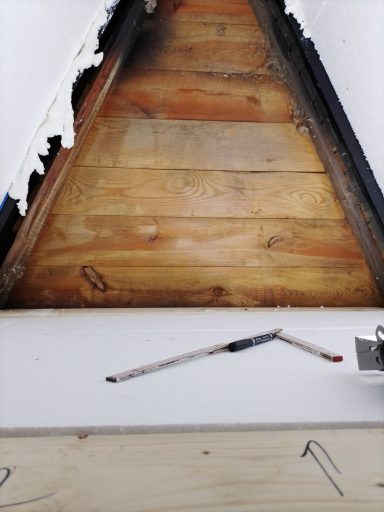 Holzverkleidung unter einem schrägen Dach mit Metallteilen und sichtbaren Nägeln.
