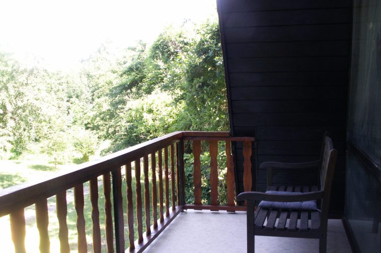 Ein Balkon mit Holzgeländer und einem Stuhl, umgeben von grüner Vegetation.