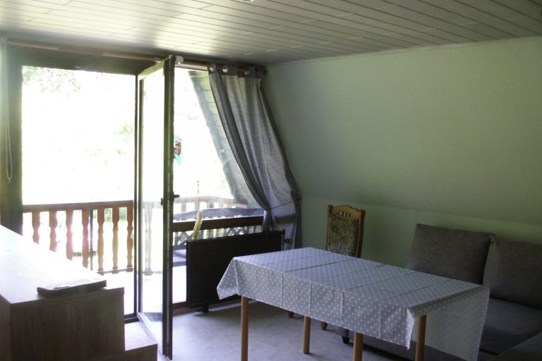 Heller Wohnraum mit Tisch, Stühlen und einer offenen Balkontür.