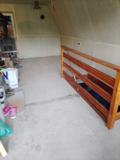 Holzregal in einem unmöblierten Raum mit Betonboden und grauen Wänden.