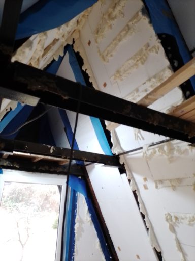 Abgerissene Wand mit freiliegenden Balken und isolierender Schaumstoffdämmung.
