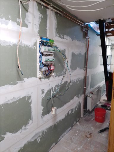 Unfertige Wand mit Leitungen und Stromverteiler in einem Raum.