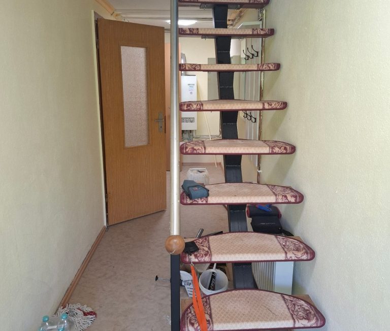 Flur2 Holztreppe mit gelben Wänden und einer offenen Tür am Ende des Flurs.