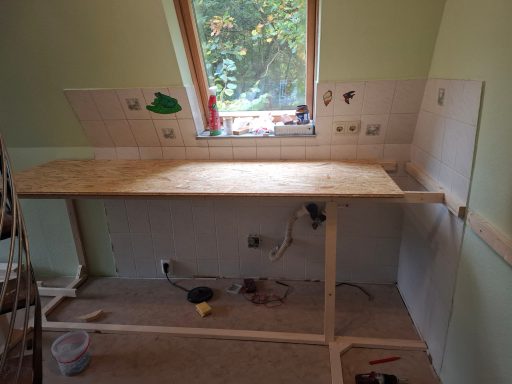 Holztisch in einem Raum, unvollständig, mit teilweise verputzten Wänden und Kabeln.