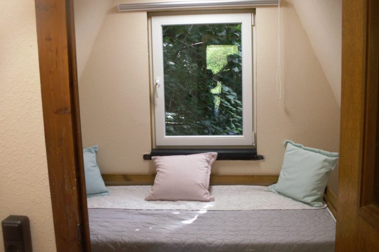 Gemütliche Bett mit Kissen neben einem Fenster mit Blick ins Grüne.